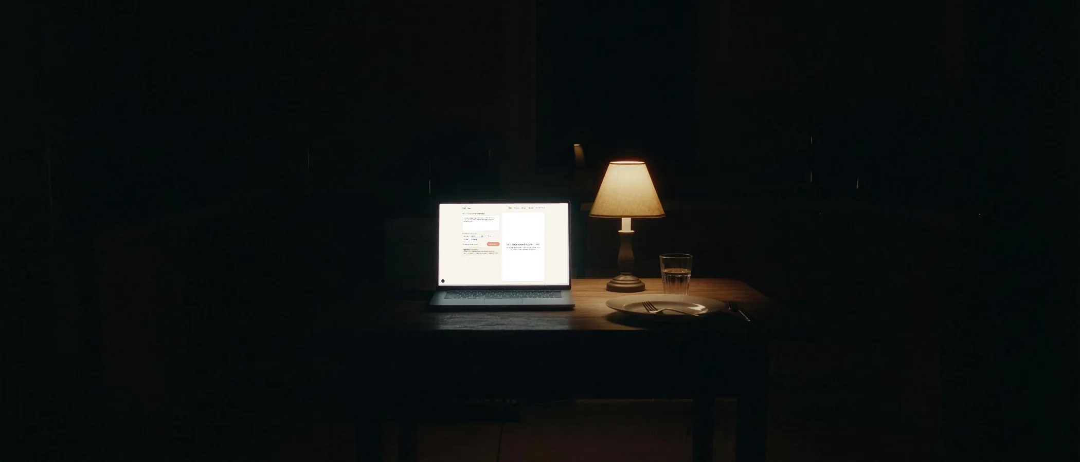 A kitchen table at night, a laptop open to the empty Loft prompt field, a lamp, an empty plate pushed aside.
