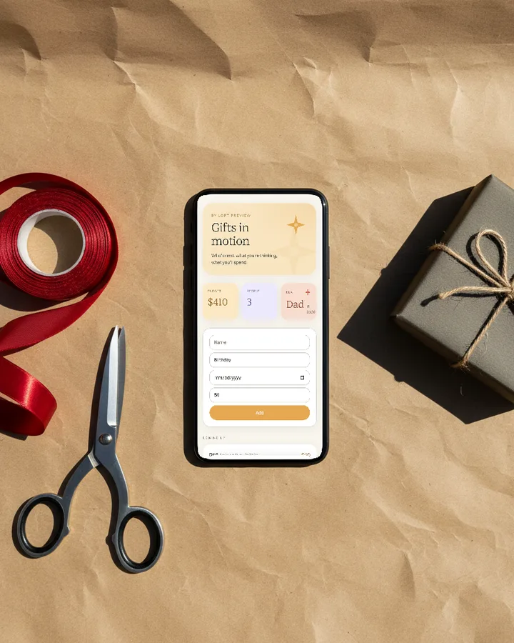 The Gift Planner app on a phone laid on kraft wrapping paper beside red ribbon and scissors, photographed from above.