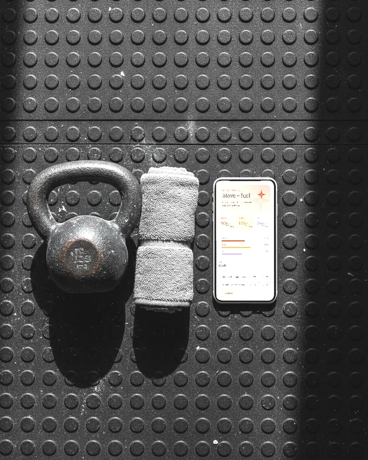 The Workout & Macros app on a phone laid on a rubber gym floor beside a kettlebell, photographed from above.